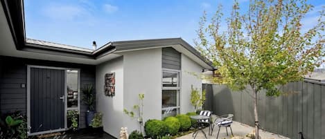 A modern house with a dark front door, a small porch, and a garden with a tree and shrubs.