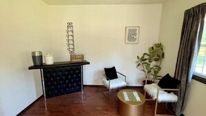 Una stanza con un divano nero capitonné, un tavolino rotondo, una poltroncina nera, una pianta in vaso e un oggetto decorativo a parete.