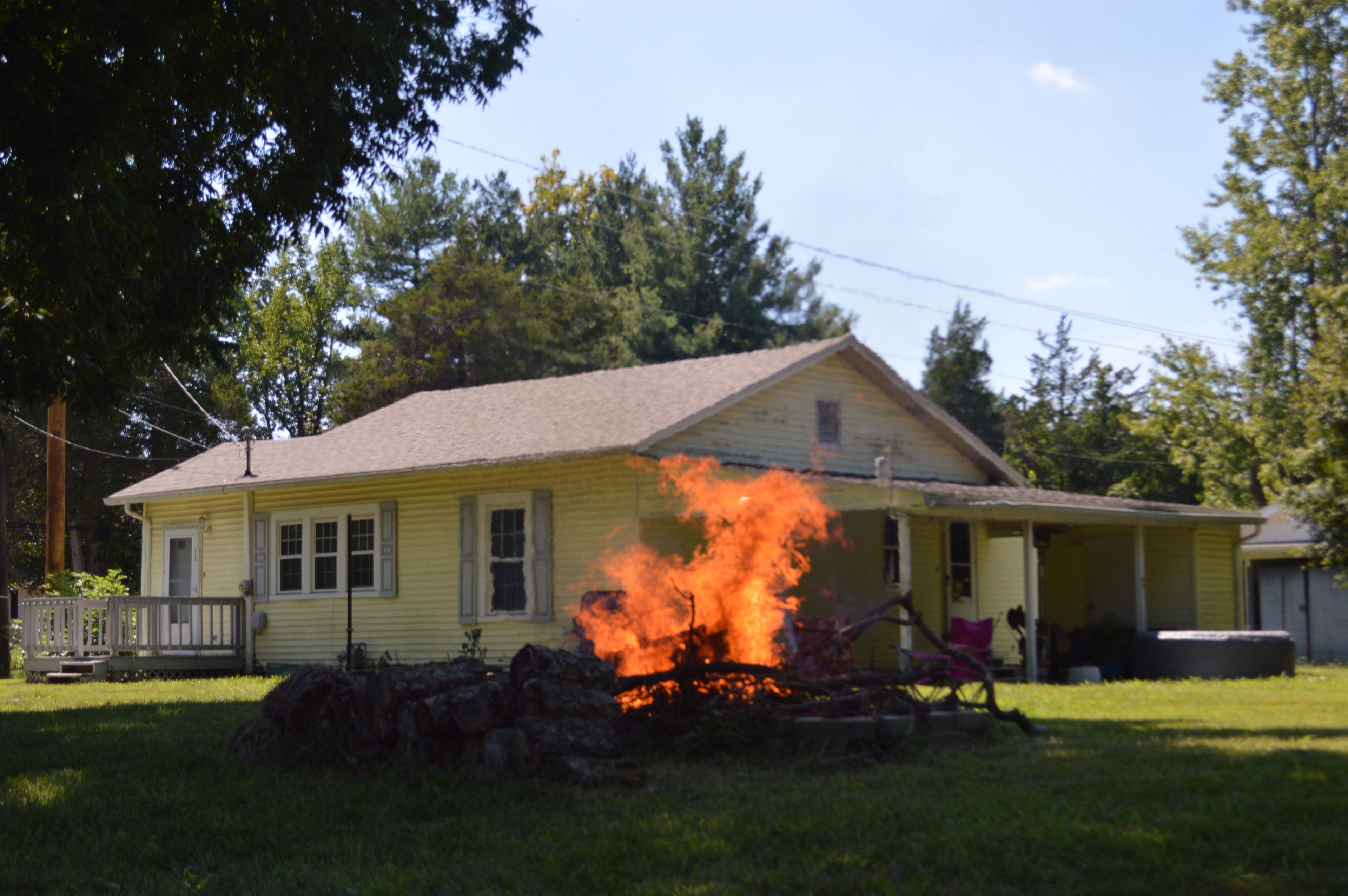 A yellow house with a fire in the front yard.