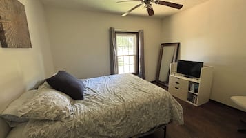 Ein Schlafzimmer mit einem Bett, einem Schminktisch, einem Fernseher und einem Deckenventilator.