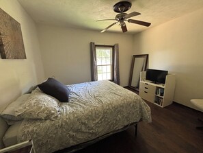Quarto com cama, penteadeira, televisão e ventoinha no teto.
