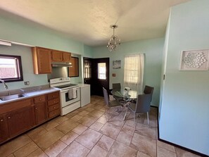 A kitchen with wooden cabinets, a stove, and a dining table with chairs. - The Lux Collective- Private Hot Tub, Dry Bar, 1-Acre Yard & Fire Pit (Murphysboro)