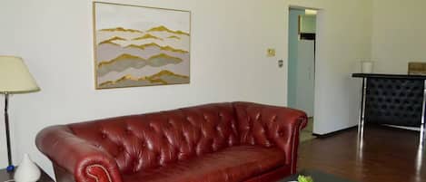 Un sofá de cuero rojo, una mesita con un control remoto y un cuadro en la pared.