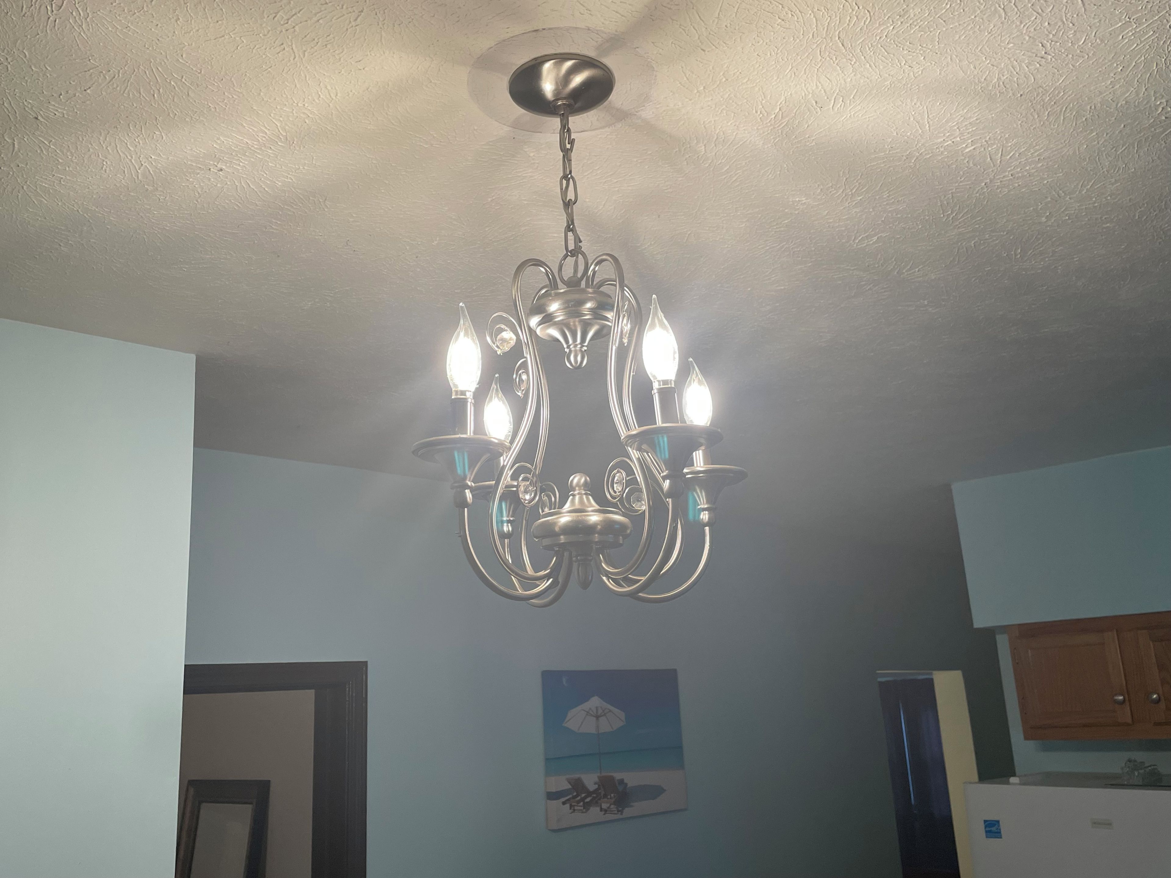 Een kroonluchter met meerdere lampen hangt aan het plafond in een kamer met lichtblauwe wanden.