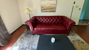 Un canapé en cuir rouge, une lampe, un tableau et une table basse dans une pièce dont le sol est recouvert d’un tapis à motifs.
