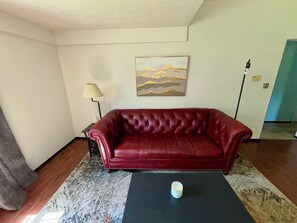 A red leather sofa, a lamp, a painting, and a coffee table in a room with a patterned rug.