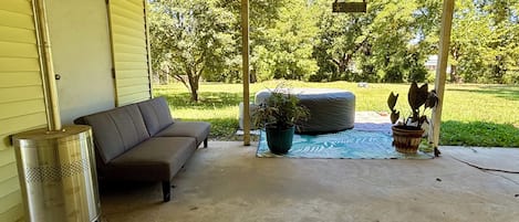 A covered porch with a sofa, a trash can, and a potted plant.