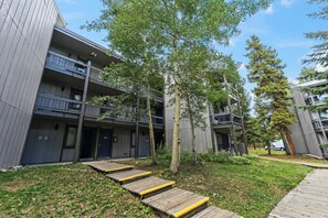 A multi-story residential building with balconies, a grassy area, and wooden steps leading to the entrance. - 5 Beds, Sleeps 8, Walkable to Peak 8 Lifts, Free Bus Outside (Breckenridge)