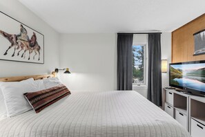A hotel room with a bed, a mounted television, a painting of horses, a window with curtains, and a view of a mountain landscape. - 5 Beds, Sleeps 8, Walkable to Peak 8 Lifts, Free Bus Outside (Breckenridge)