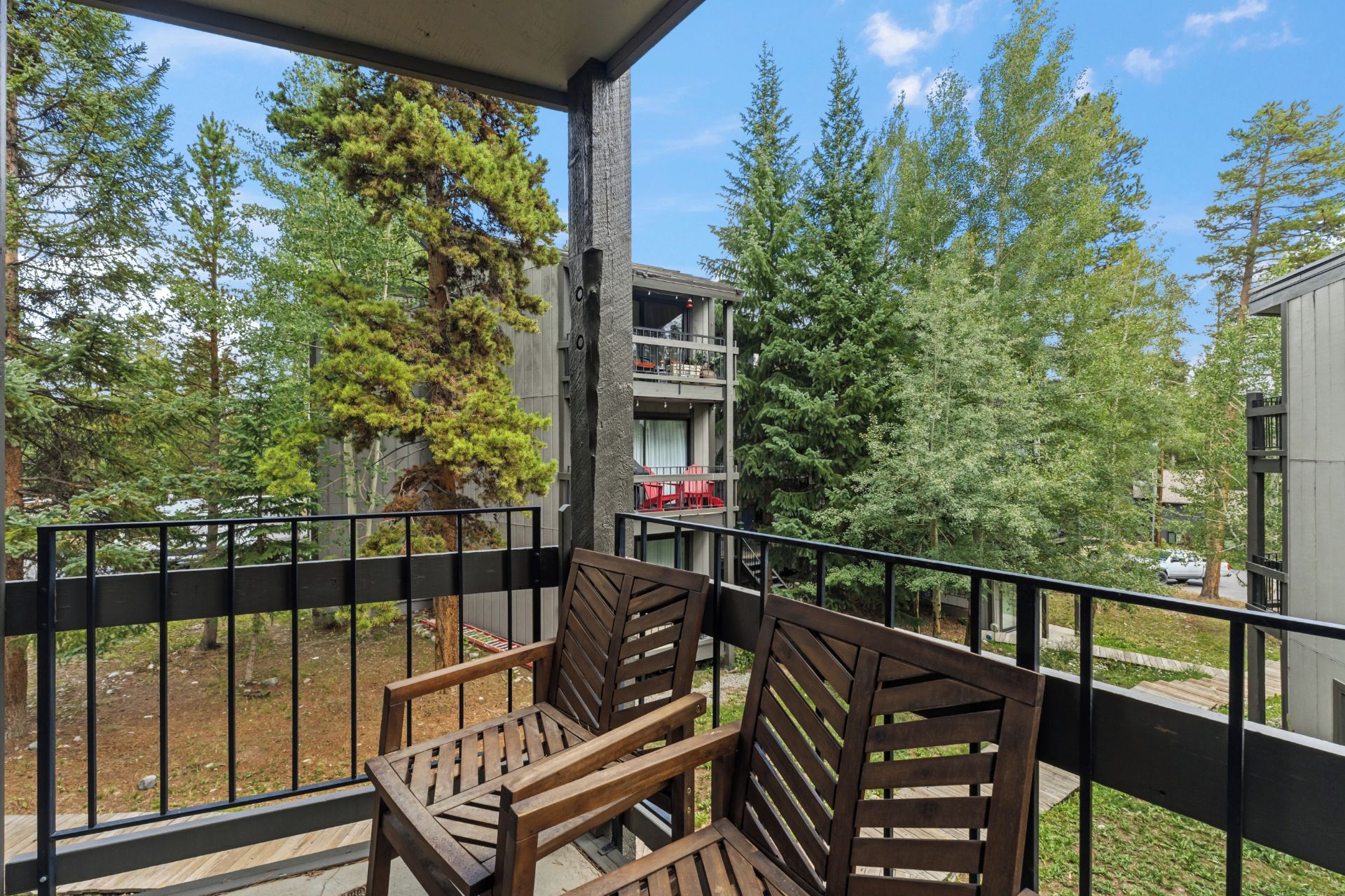 A balcony with two wooden chairs, a railing, and a view of trees and a building in the background.
