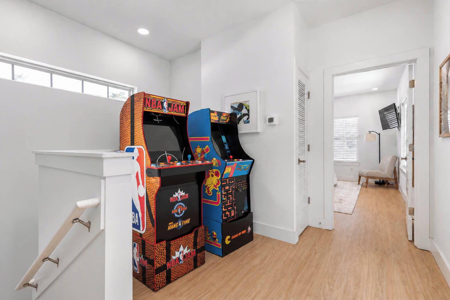 Une pièce avec deux bornes d’arcade, un mur blanc, une porte et une fenêtre.