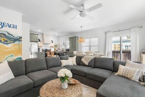 Un salon moderne avec un canapé d’angle gris, une table basse ronde en fibres tressées et un ventilateur de plafond.