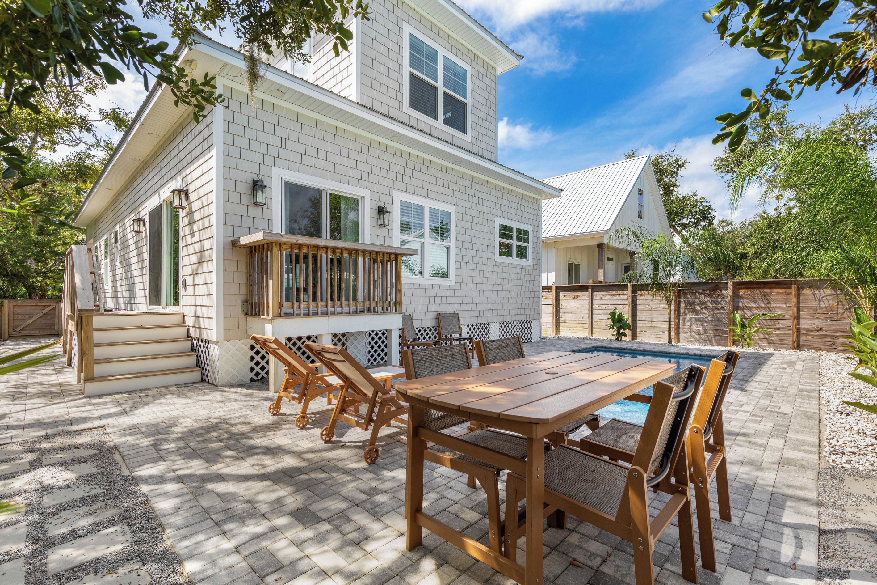Une maison à deux étages dotée d’un patio comprenant une table et des chaises en bois, une piscine et un jardin clôturé.