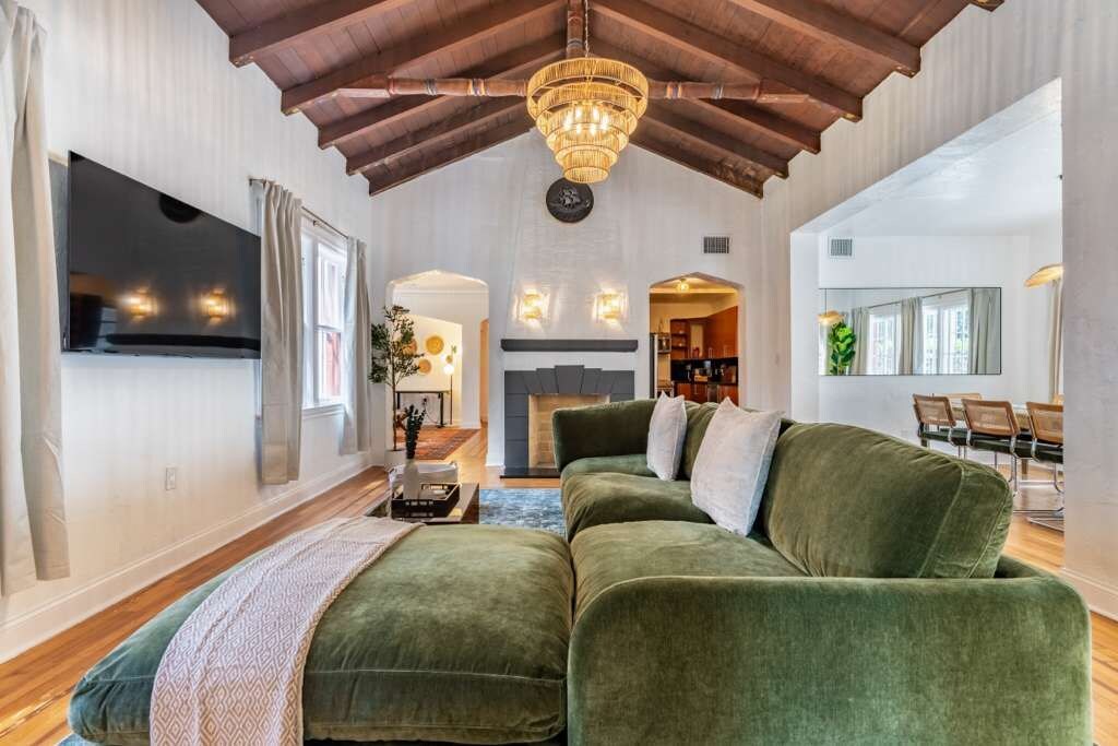 A spacious living room with a high ceiling, a green sofa set, and a chandelier.