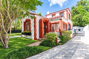 A two-story house with a red and white exterior, a front porch, and a well-maintained garden. - 5 Bedroom | Home Near Wynwood | Pool |Free Parking (Miami)