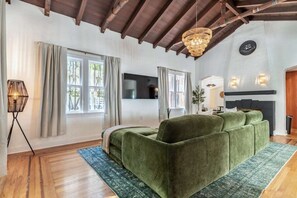 A living room with a green sofa, wooden flooring, a chandelier, and a fireplace. - 5 Bedroom | Home Near Wynwood | Pool |Free Parking (Miami)