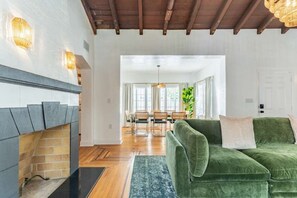 Ein Wohnzimmer mit einem grünen Sofa, einem Kamin und einem Essbereich im Hintergrund.