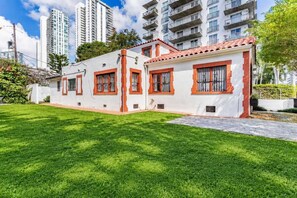 A two-story building with a flat roof and red-framed windows, surrounded by a well-maintained lawn and tall residential buildings in the background. - 5 Bedroom | Home Near Wynwood | Pool |Free Parking (Miami)