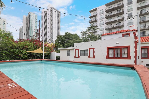 A swimming pool with a wooden deck, surrounded by a building with red window frames and a white facade. - 5 Bedroom | Home Near Wynwood | Pool |Free Parking (Miami)