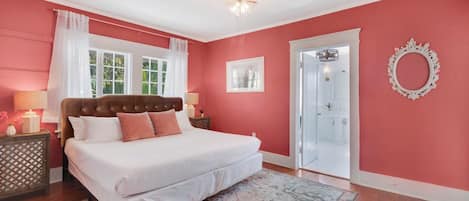 A bedroom with a large bed, a bedside table, a nightstand, a rug, a door, and a mirror on the wall.