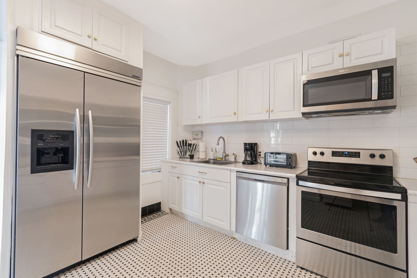 A modern kitchen with stainless steel appliances, white cabinetry, and a patterned floor.