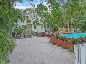Um quintal com piscina, deck de madeira e área de estar coberta.