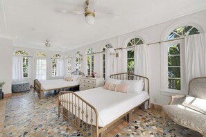 A spacious bedroom with two beds, a large window, and a ceiling fan.