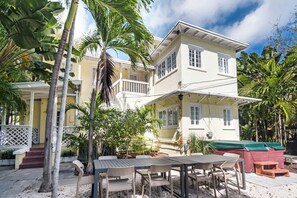 A two-story building with a balcony, surrounded by palm trees and a patio area with outdoor furniture.