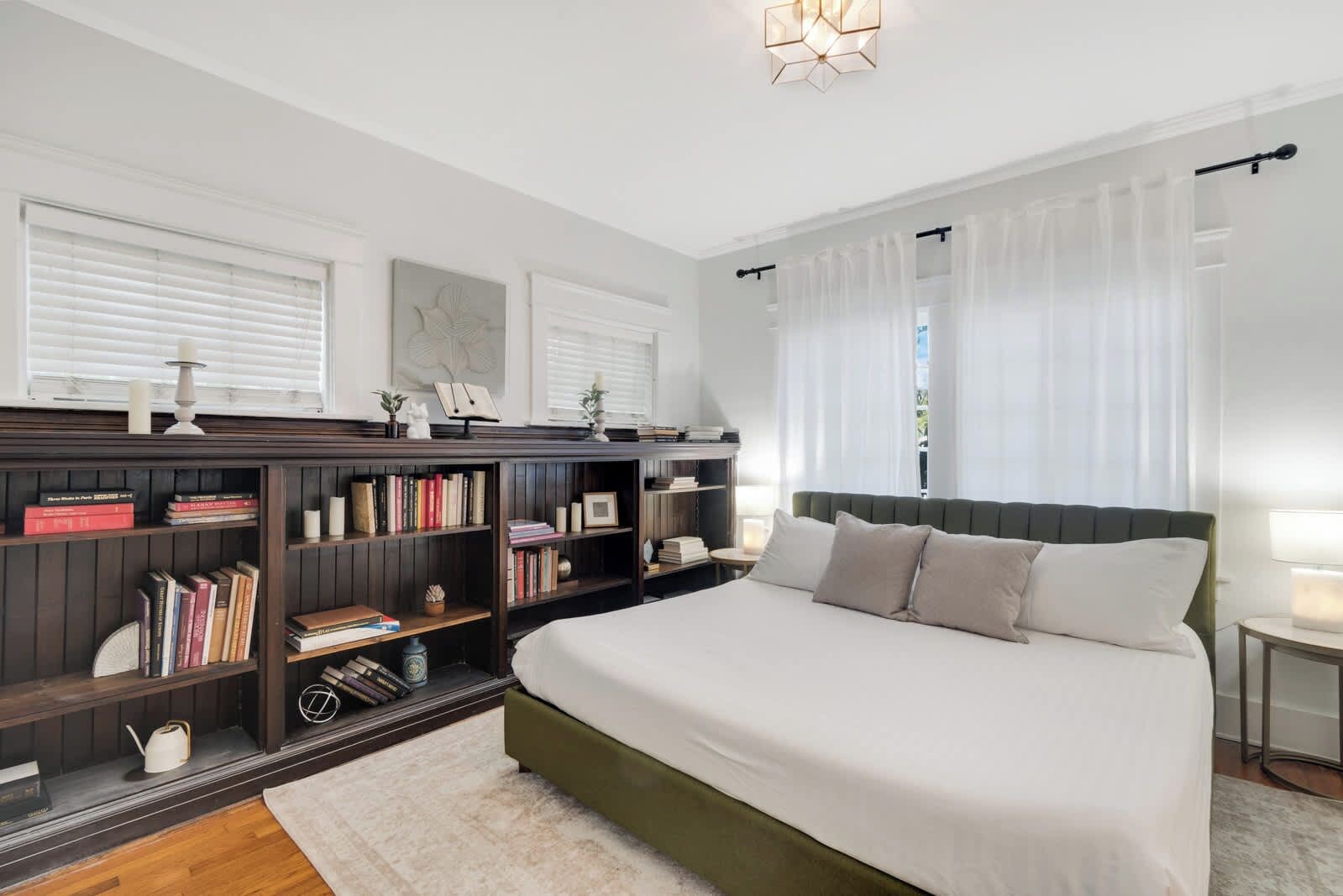 A bedroom with a large bed, a bookshelf, and a window with curtains.
