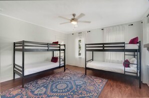 Quarto com duas camas de solteiro sobrepostas, ventoinha no teto e tapete estampado.