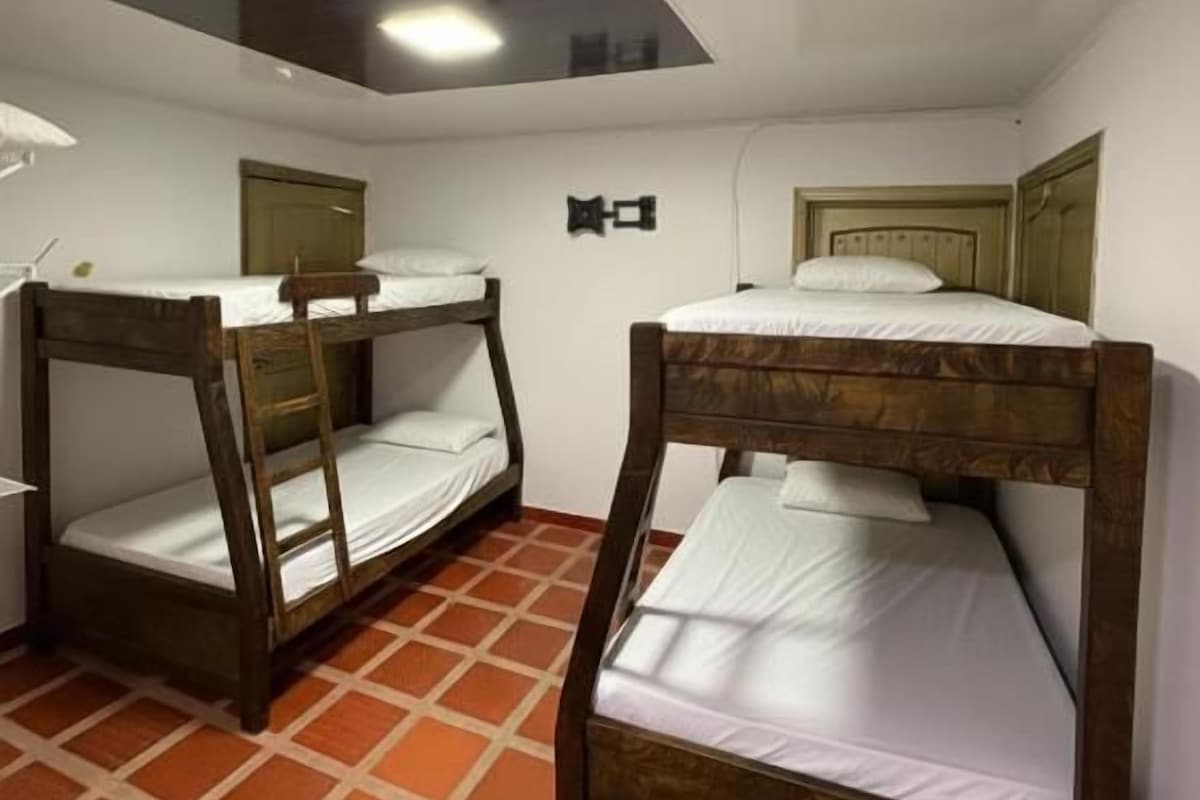 Quarto com duas beliches, uma luminária no teto e piso de azulejo.