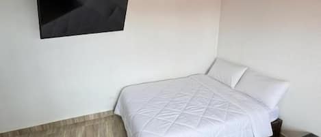 Une chambre à coucher avec un lit, un téléviseur fixé au mur et un plancher en bois.