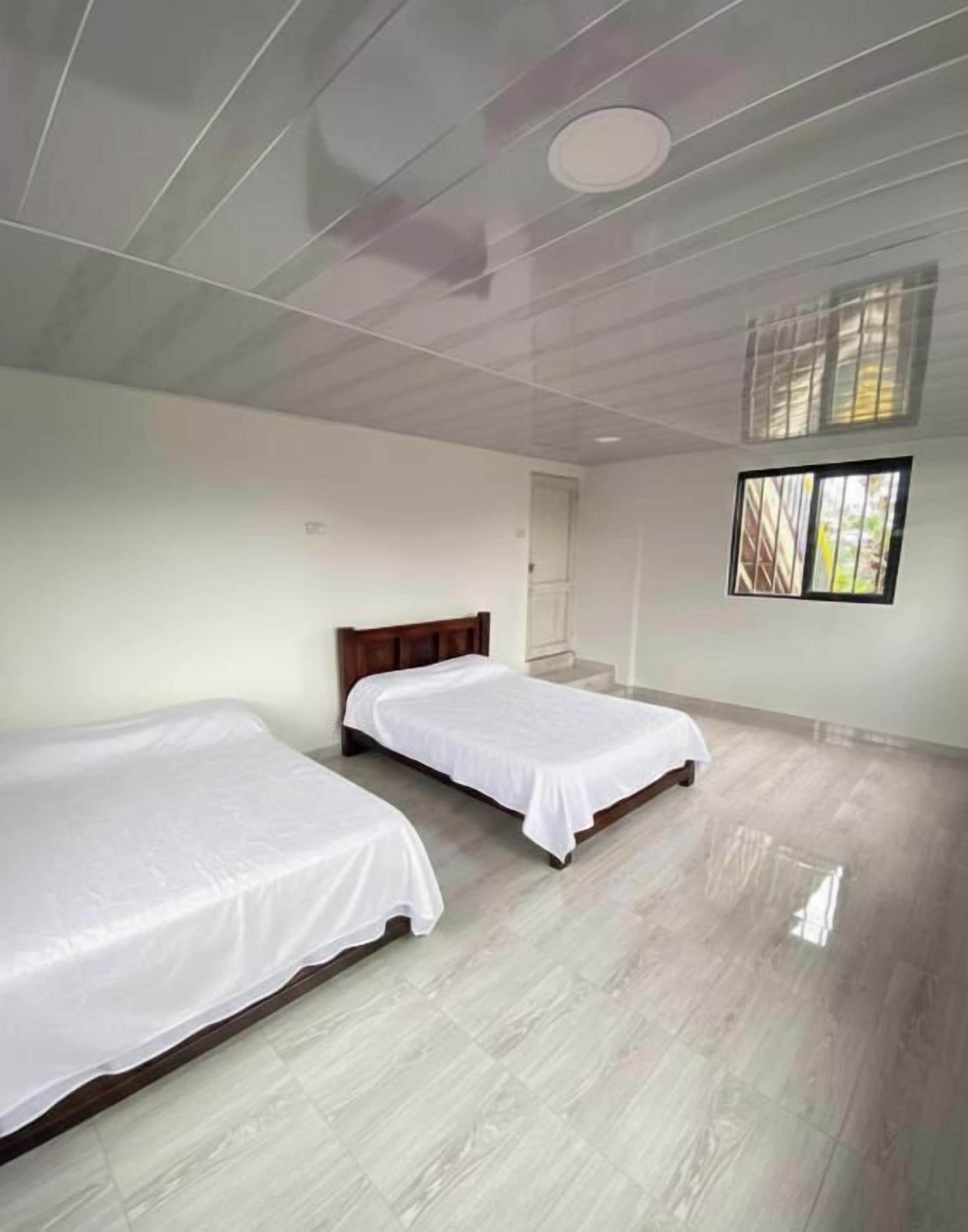 A room with two beds, a wooden headboard, a window with blinds, and a door.