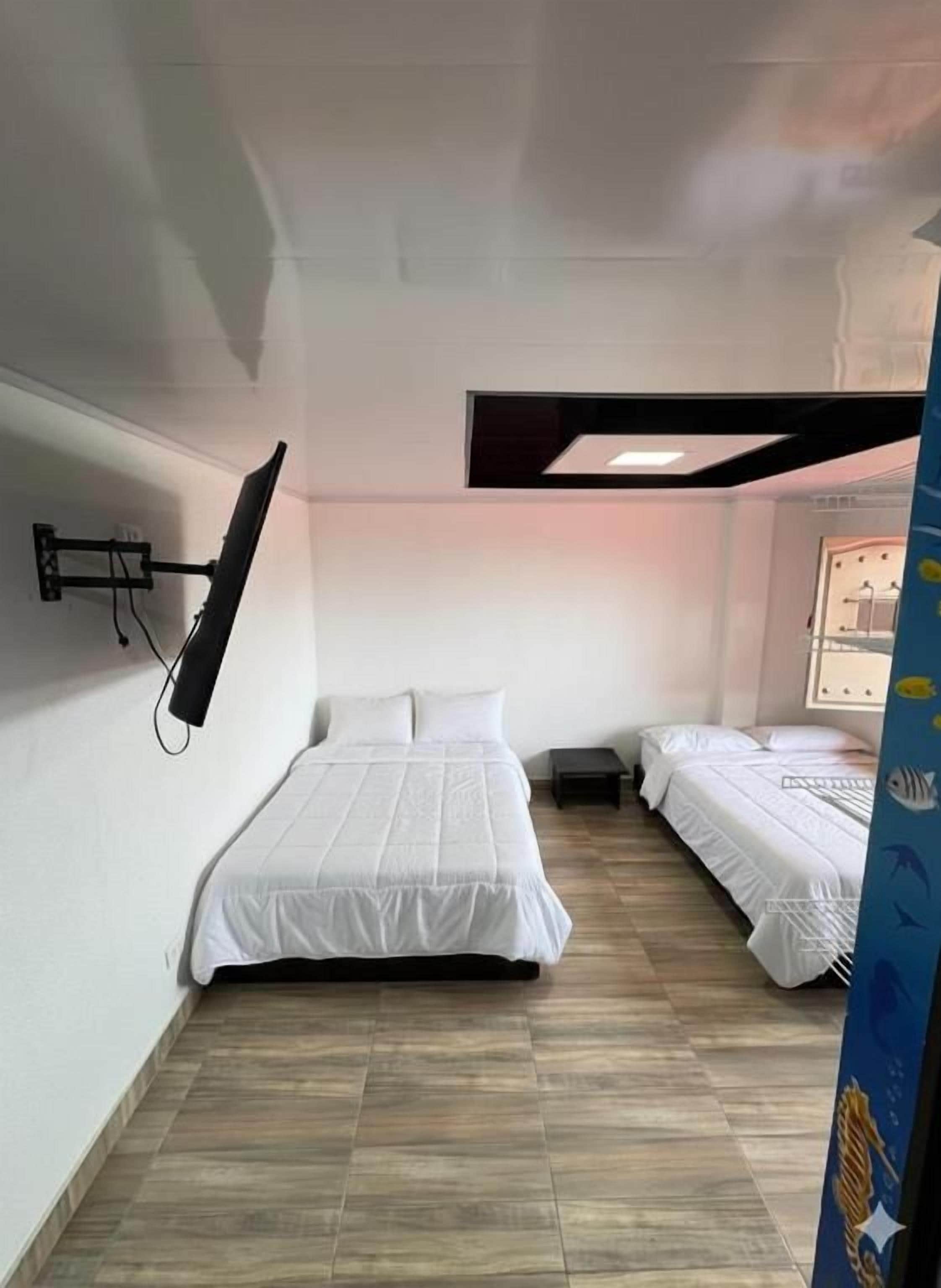 Quarto com duas camas, televisão de tela plana na parede e janela com cortinas.