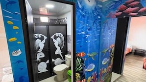 Une salle de bain ornée d’une fresque représentant un paysage sous-marin, avec des toilettes et un lavabo.