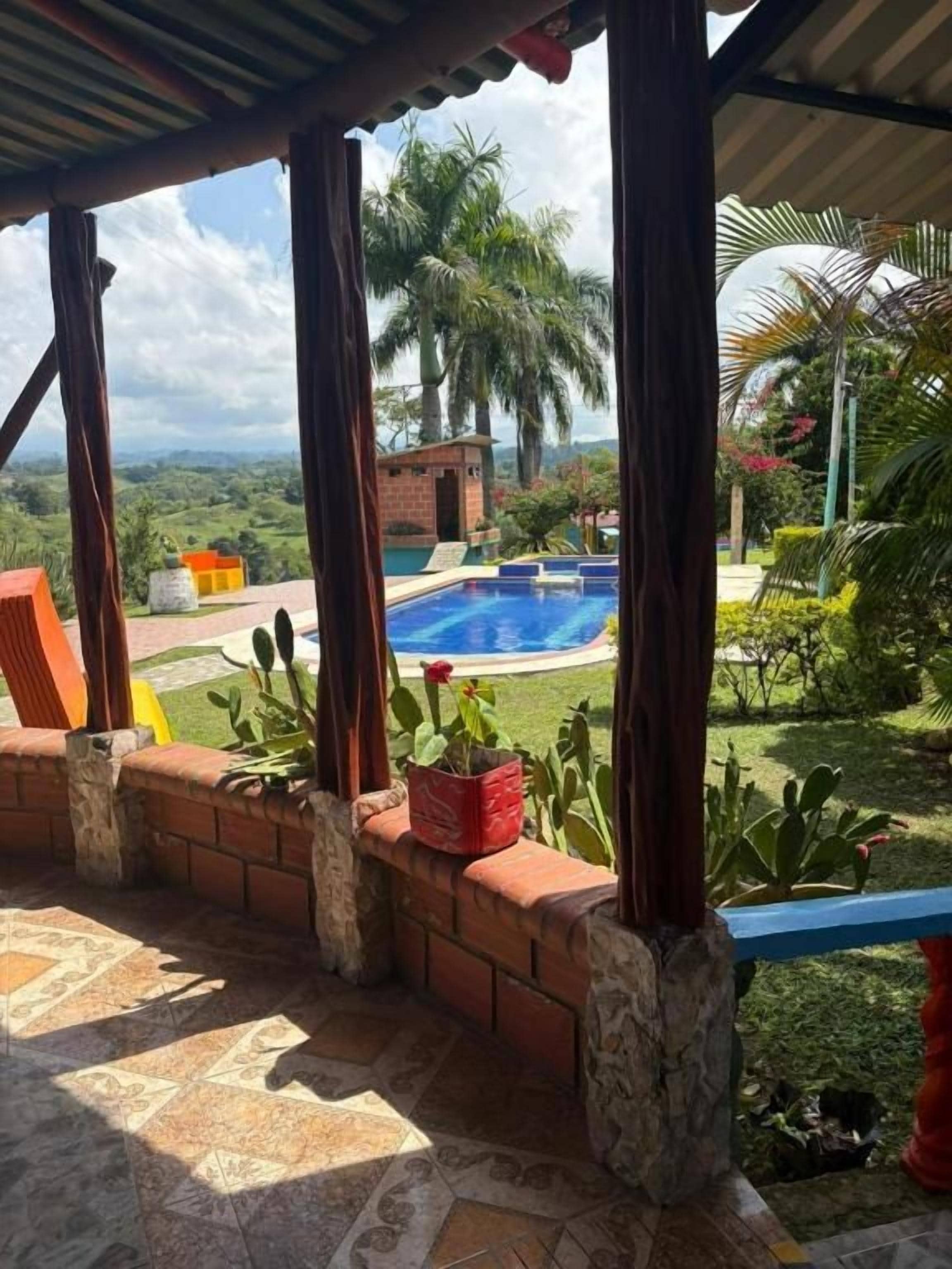 A covered patio with a pool, brick walls, and a view of a lush landscape.
