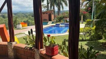 A covered patio with a pool, brick walls, and a view of a lush landscape.