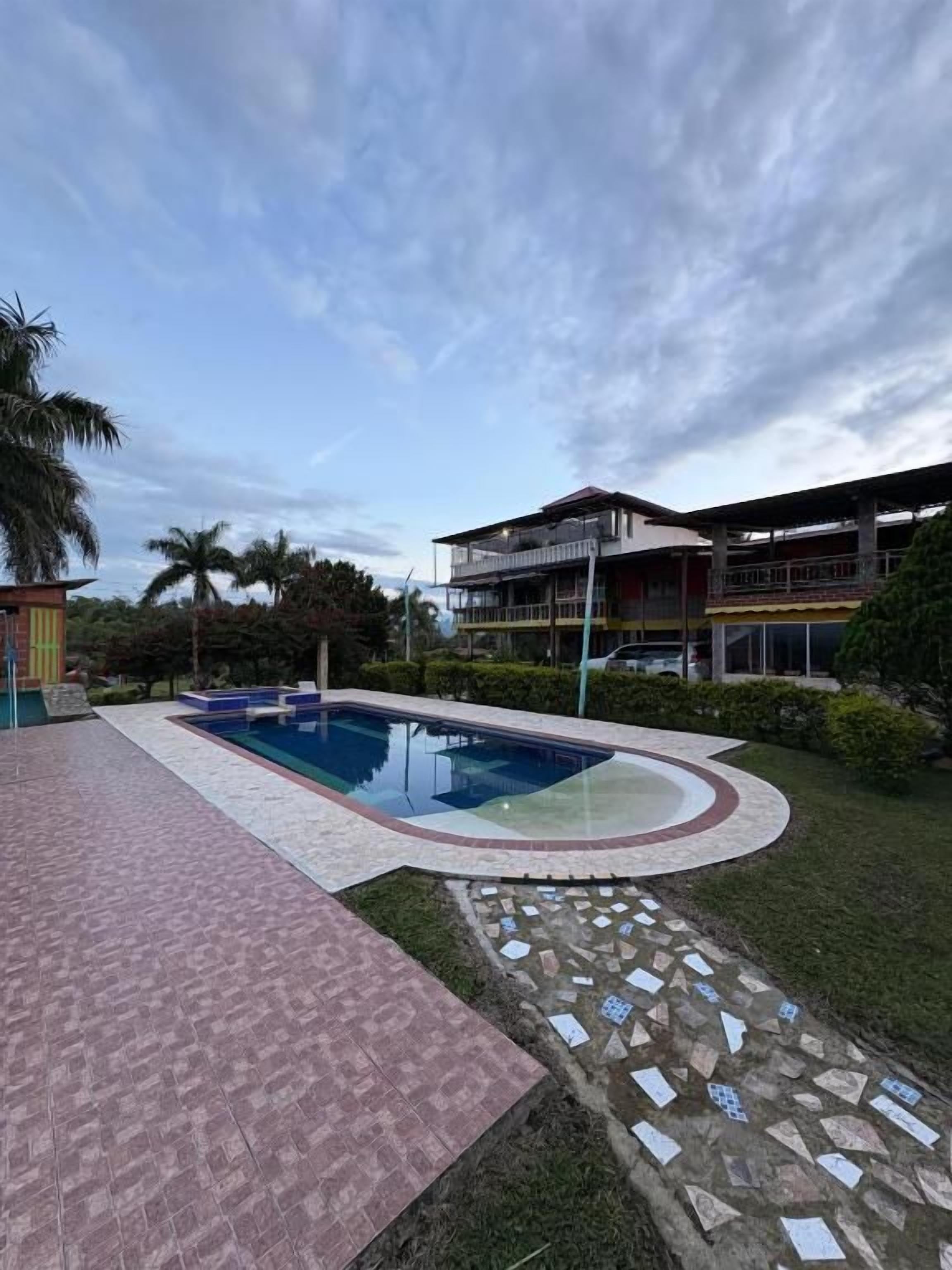 Una piscina con suelo de baldosas, un edificio con balcón y cielo despejado.