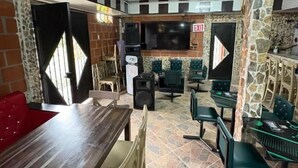 Un restaurant avec une longue table en bois, plusieurs chaises, un écran de télévision et un pilier en pierre.