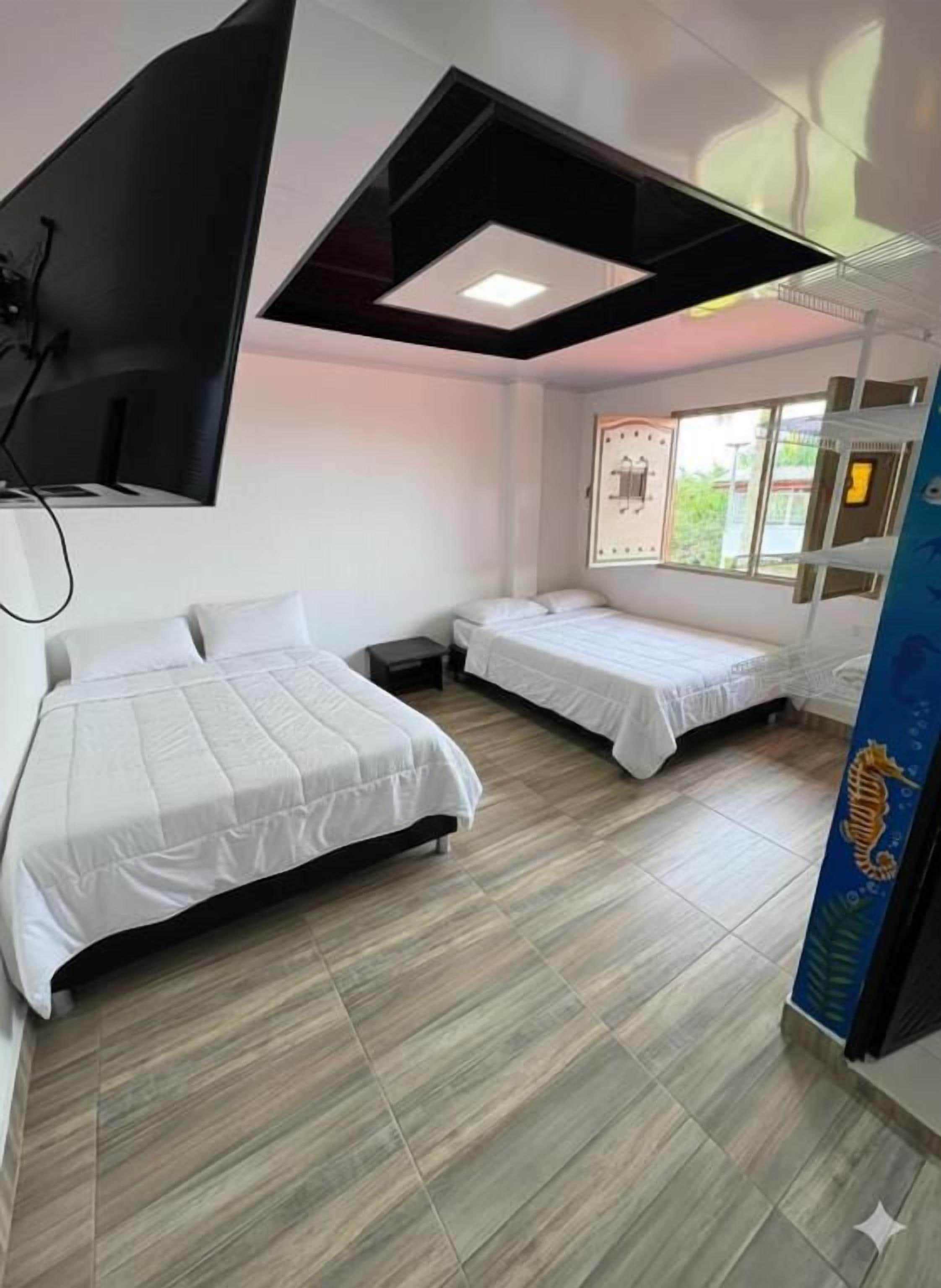 Habitación de hotel con dos camas, un televisor de pantalla plana montado en la pared y una ventana con vistas al exterior.