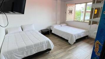 Habitación de hotel con dos camas, un televisor de pantalla plana montado en la pared y una ventana con vistas al exterior.