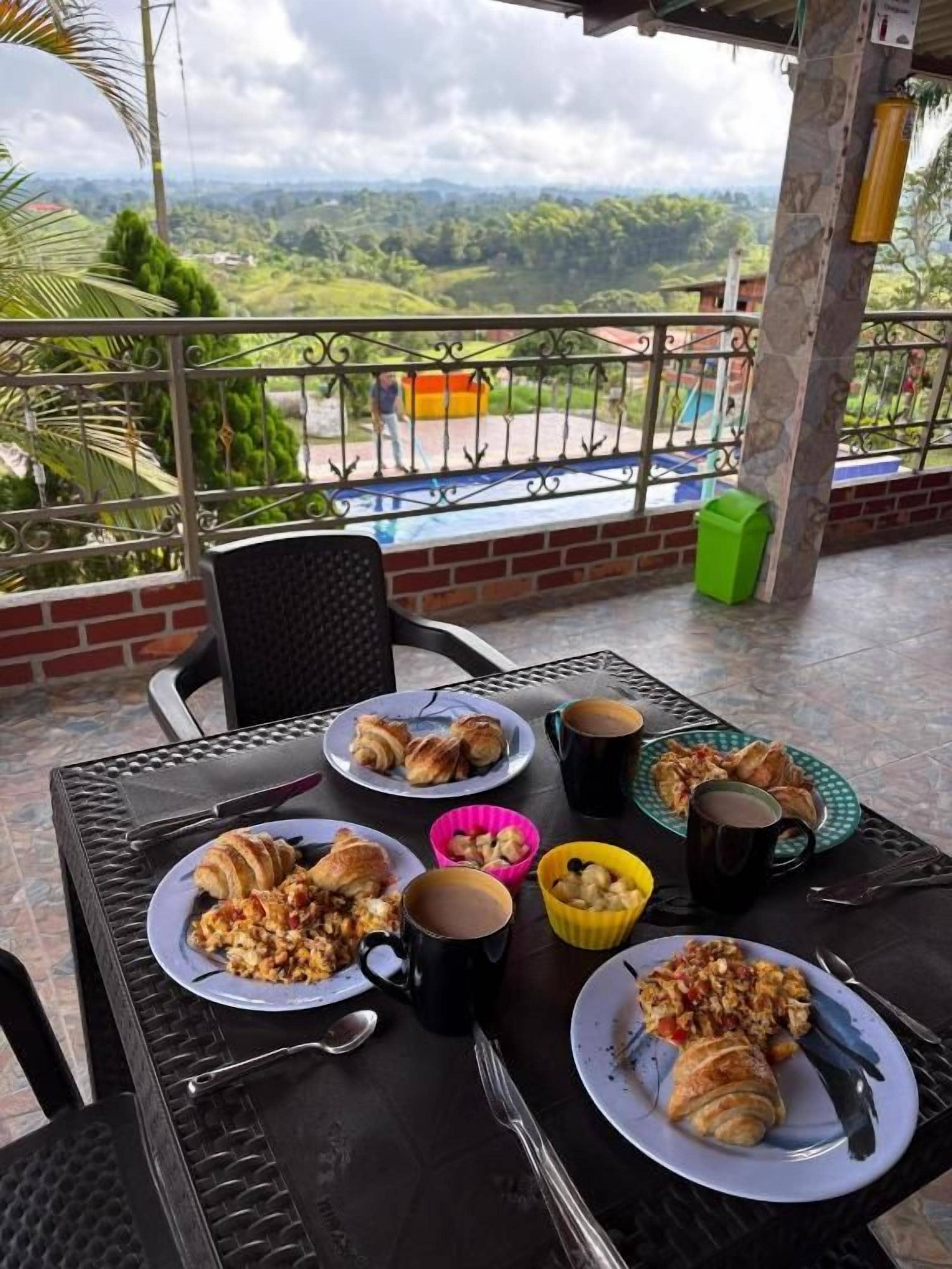 Mesa de jantar com pratos de comida, copos e talheres numa varanda com vista para a paisagem.