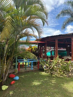 A covered outdoor area with a wooden structure, palm trees, and colorful spherical objects on the ground. - Rancho Akila (Filandia)