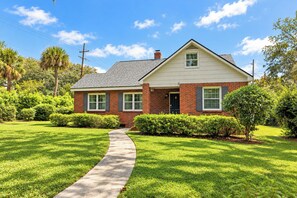 A two-story brick house with a front porch, a clear pathway leading to the entrance, and well-maintained green lawns. - 2bd/2ba Home * Renovated * 30+ Day Stay (Savannah)