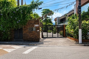 A gated entrance with a brick wall and a number '280' sign, leading to a modern building with glass windows and a metal gate. - Villaggio Arcobaleno (São Sebastião)