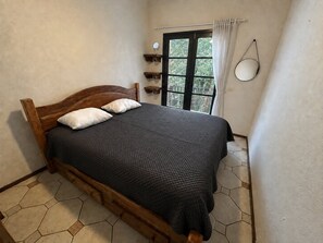 A room with a bed, a window with curtains, a mirror, and a view of greenery outside. - Villaggio Arcobaleno (São Sebastião)