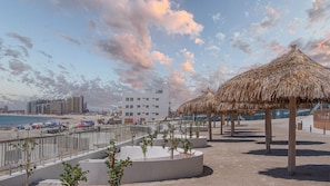 Een strandresort met een paviljoen met rieten dak, een zwembadgedeelte met palmbomen en uitzicht op de oceaan en de stadshemel.