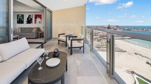A balcony with a sofa, chairs, a table with a wine glass and plate, and a cityscape view. - One 1702 Penthouse: Star Wars Oceanfront Penthouse| Sonoran Star Resort ⭐🌊 (Puerto Peñasco)