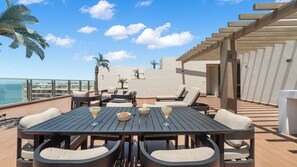 Une terrasse extérieure avec une table en bois, des chaises et une vue sur l’océan.