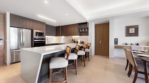 A modern kitchen with a central island, bar stools, stainless steel appliances, and a dining area with a table and chairs. - One 1702 Penthouse: Star Wars Oceanfront Penthouse| Sonoran Star Resort ⭐🌊 (Puerto Peñasco)